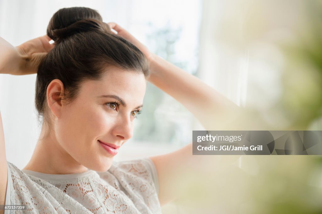 Caucasian woman tying hair in bun