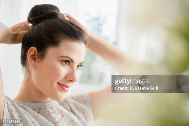 caucasian woman tying hair in bun - hair bun stockfoto's en -beelden