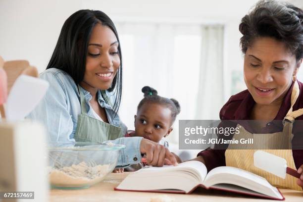 black multi-generation family reading recipe in cookbook - baking reading recipe stockfoto's en -beelden