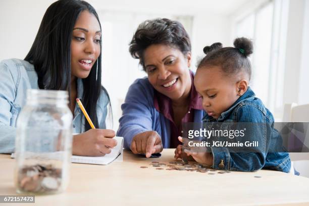 black multi-generation family counting coins - 50s woman writing at table stock-fotos und bilder