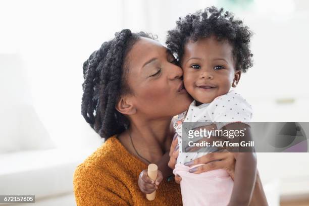 smiling black mother kissing baby daughter on cheek - mother and daughter kiss happy stock-fotos und bilder