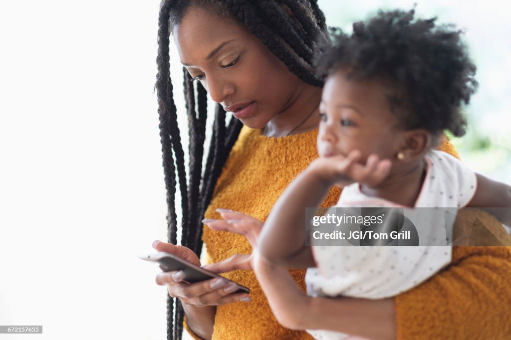 Black woman holding baby daughter using cell phone