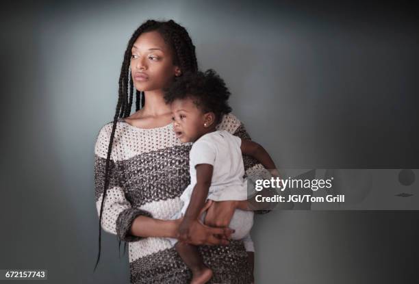 thoughtful black woman standing holding baby daughter - mother holding baby stockfoto's en -beelden