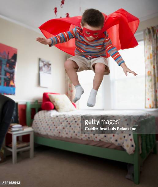 mixed race boy wearing superhero costume jumping off bed - flowing cape 個照片及圖片檔