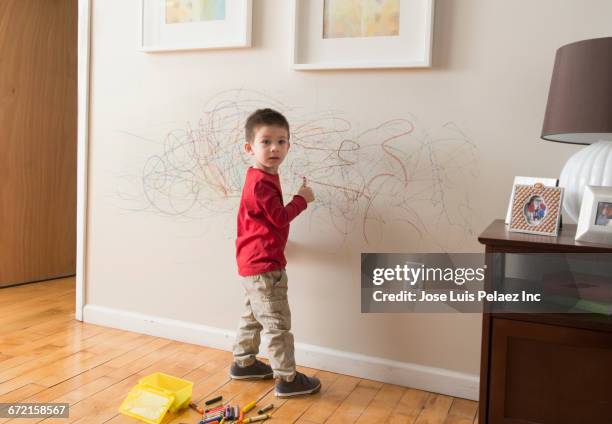 mixed race boy drawing on wall with crayons - kind staunen stock-fotos und bilder