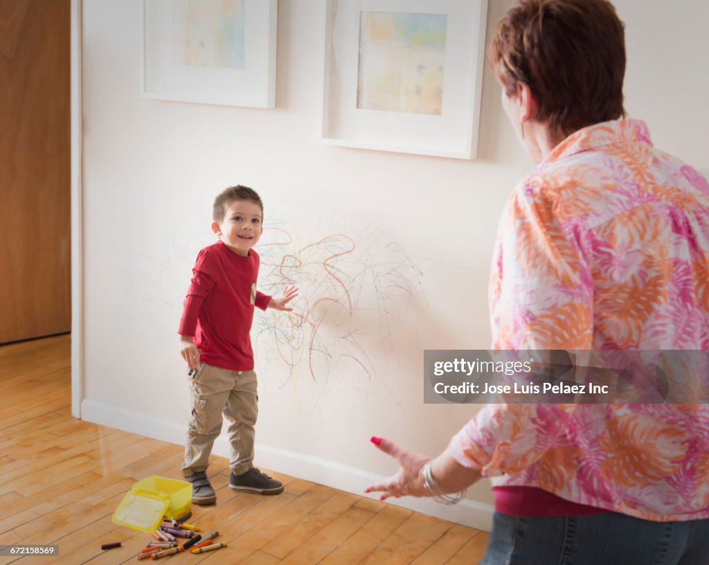 Grandmother angry at grandson drawing on wall with crayons