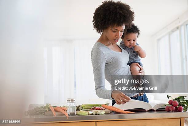 mother reading cookbook while holding baby son - cooking cookbook stock pictures, royalty-free photos & images
