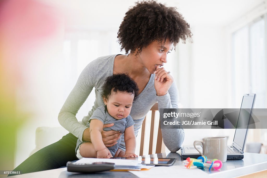 Mother holding baby son worrying about laptop