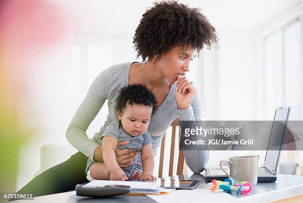 mother holding baby son worrying about laptop - millennial generation stock-fotos und bilder