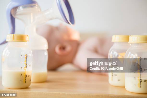 caucasian baby boy laying near bottles of breast milk and breast pump - milk pumping stockfoto's en -beelden