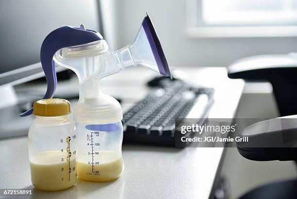 breast pump and bottle of breast milk near computer - milk pumping stockfoto's en -beelden