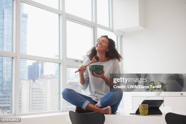 mixed race woman eating chocolate from bowl with wooden spoon - schneidersitz stock-fotos und bilder