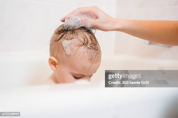 caucasian mother washing hair of baby daughter in bathtub - mother and baby taking a bath stock pictures, royalty-free photos & images