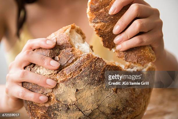 hispanic woman tearing round loaf of bread - backwaren stock-fotos und bilder