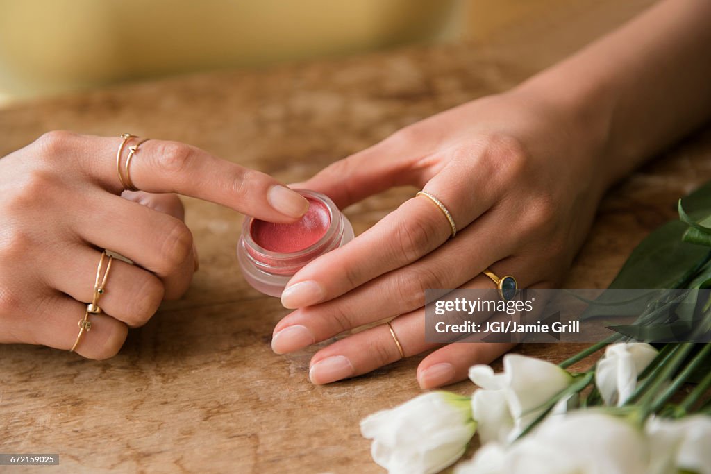 Hands of Hispanic woman holding jar of lip gloss