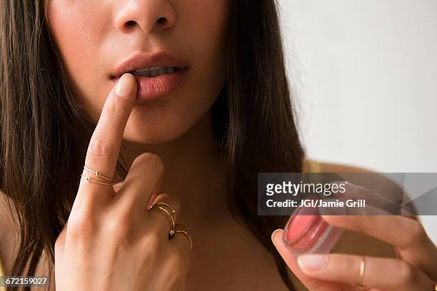 hispanic woman applying lip gloss - finger on lips stock-fotos und bilder