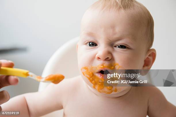 mother feeding messy baby son with spoon in high chair - baby eating food imagens e fotografias de stock