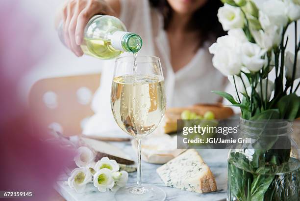 hispanic woman pouring wine at table - chardonnay grape stock pictures, royalty-free photos & images
