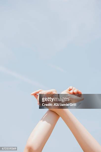 hispanic woman crossing arms at wrist under blue sky - handgelenk stock-fotos und bilder