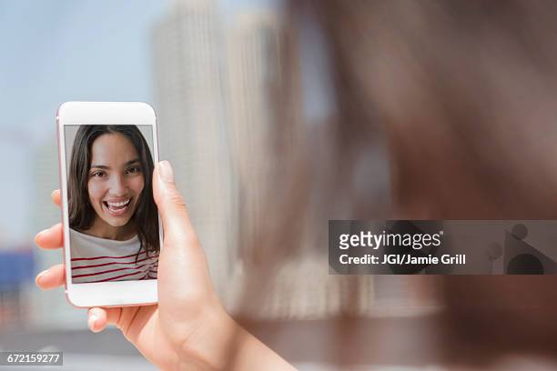 smiling hispanic woman posing for cell phone selfie - femme de dos smartphone photos et images de collection