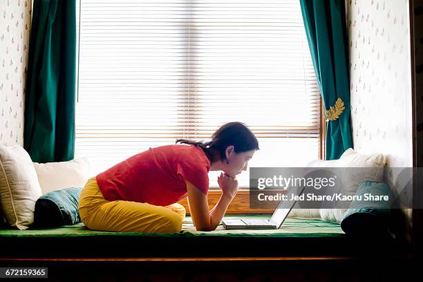 japanese woman leaning on day bed reading laptop - red tour fotografías e imágenes de stock