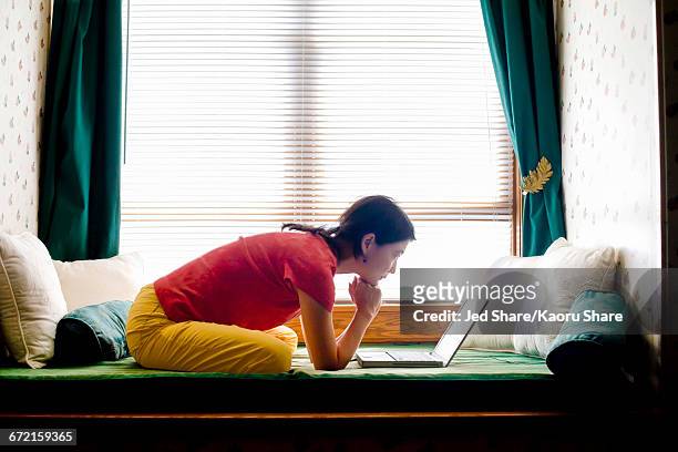 japanese woman leaning on day bed reading laptop - chaise longue - fotografias e filmes do acervo