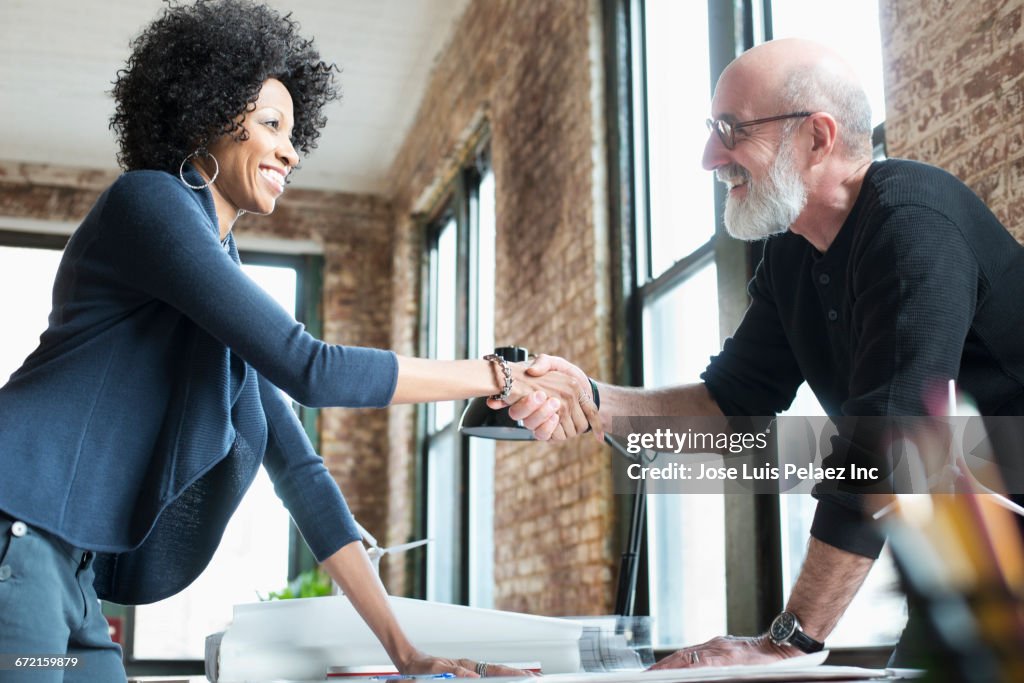 Business people handshaking over blueprints on desk