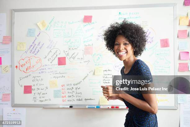 laughing black businesswoman making presentation at whiteboard - woman whiteboard fotografías e imágenes de stock
