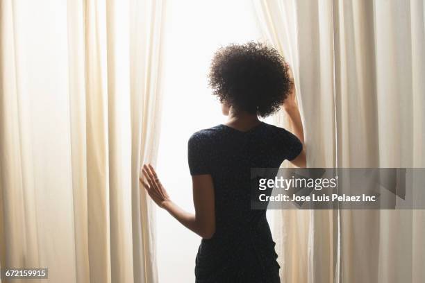 black businesswoman opening curtain at window - black dress stock pictures, royalty-free photos & images