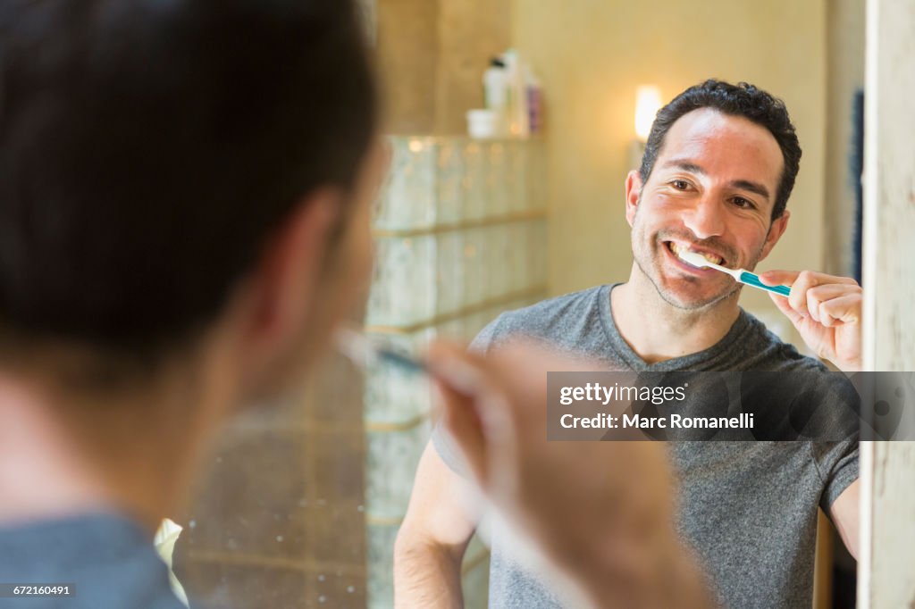 Hispanic man brushing teeth in mirror