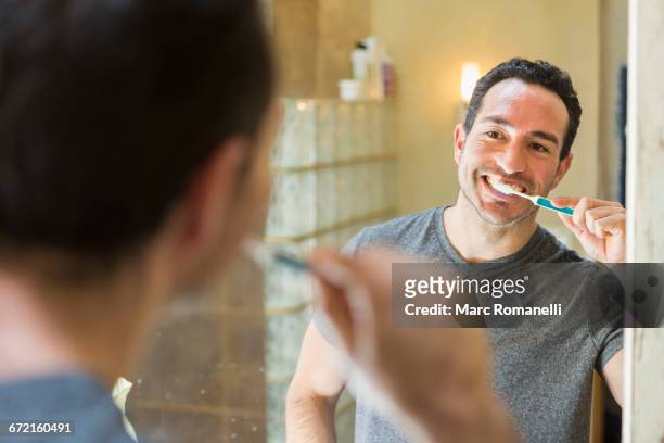 hispanic man brushing teeth in mirror - toothbrush stock-fotos und bilder