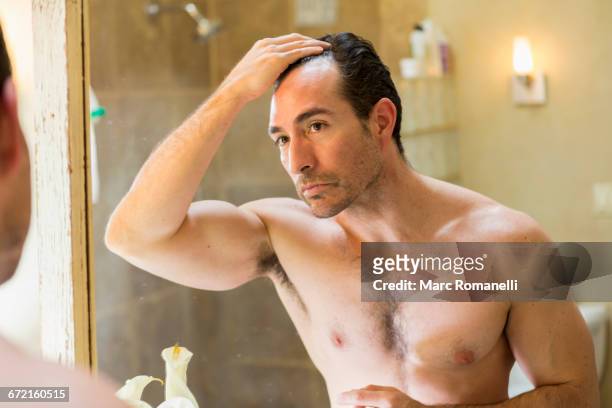 hispanic man checking receding hairline in mirror - haare mann stock-fotos und bilder