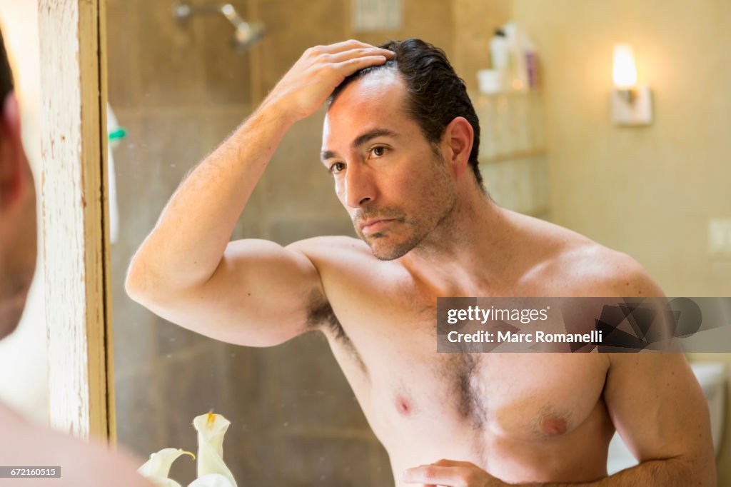 Hispanic man checking receding hairline in mirror