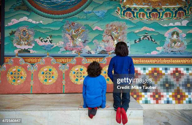 mixed race brothers kneeling on bench examining wall paintings - thimphu stock pictures, royalty-free photos & images