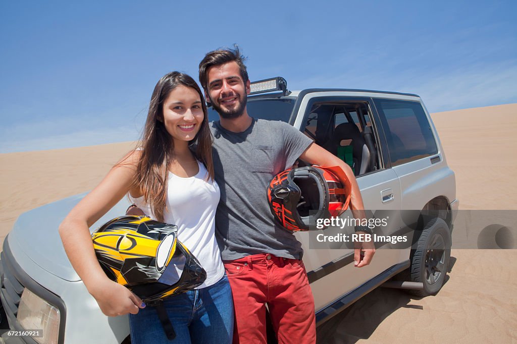 Hispanic couple holding helmets leaning on sports utility vehicle
