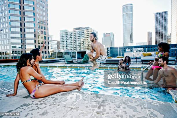 friends watching man do cannonball dive into urban swimming pool - rooftop pool imagens e fotografias de stock