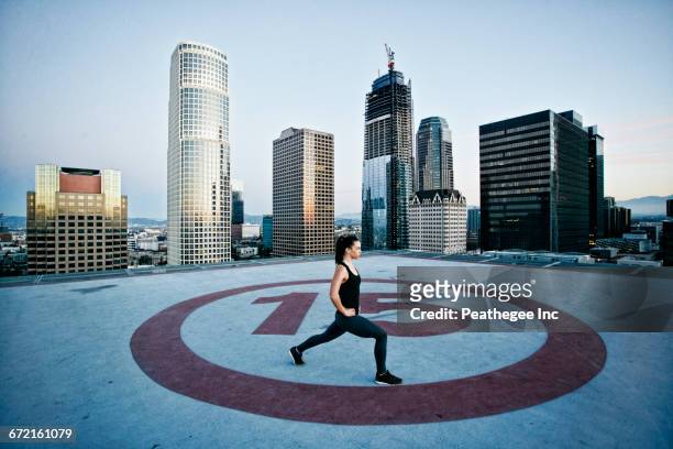 caucasian woman stretching legs on urban rooftop - helikopterplatform stockfoto's en -beelden