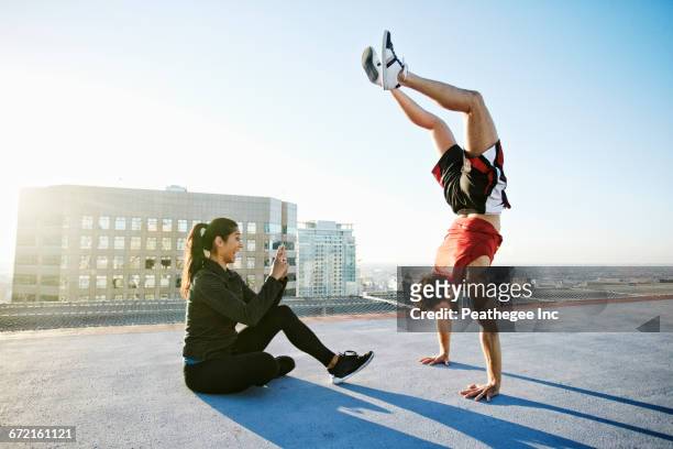 woman photographing man doing handstand on urban rooftop - fare la verticale sulle mani foto e immagini stock