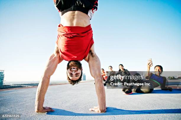 woman photographing man doing handstand on urban rooftop - équilibre sur les mains photos et images de collection