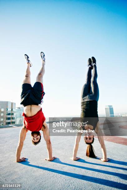 caucasian couple doing handstands on urban rooftop - fare la verticale sulle mani foto e immagini stock