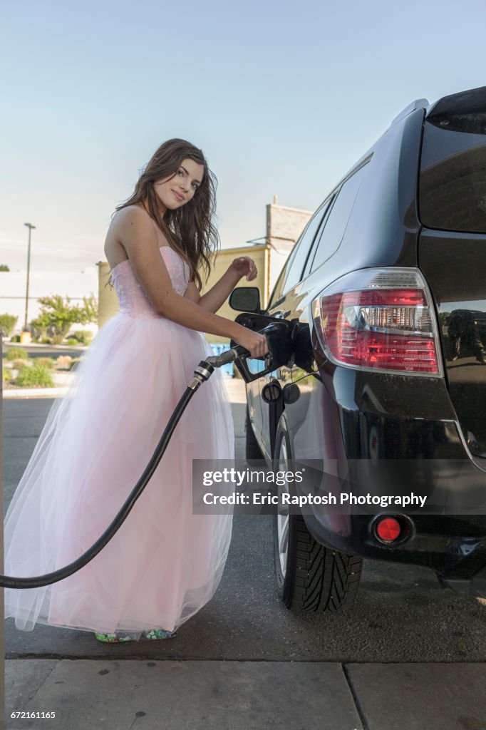 Caucasian girl wearing prom dress fueling car