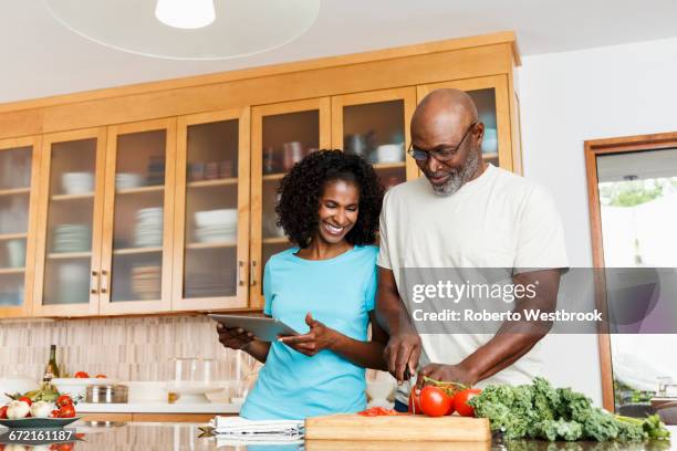 black couple with digital tablet chopping tomatoes in kitchen - baby boomer home stock pictures, royalty-free photos & images