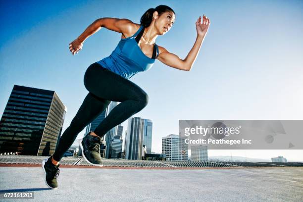 mixed race woman running on urban rooftop - sprint photos et images de collection