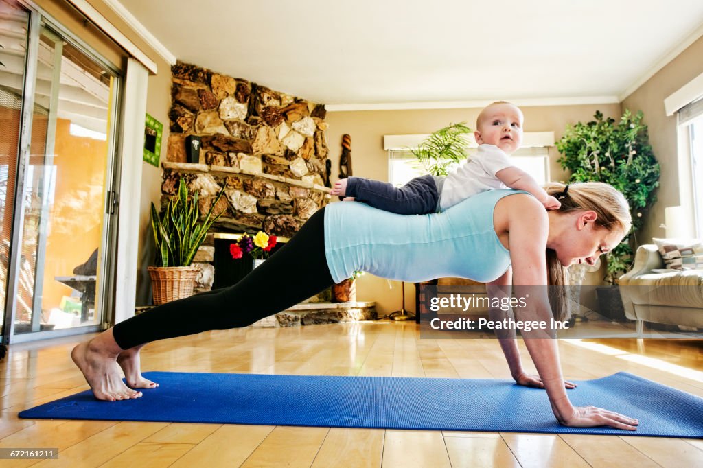 Mother working out on exercise mat with baby on back