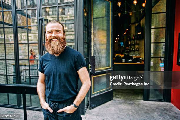 caucasian man with beard smiling on sidewalk - bar outside stock-fotos und bilder