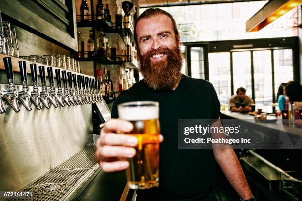 smiling caucasian bartender serving beer at bar - holding beer stock pictures, royalty-free photos & images