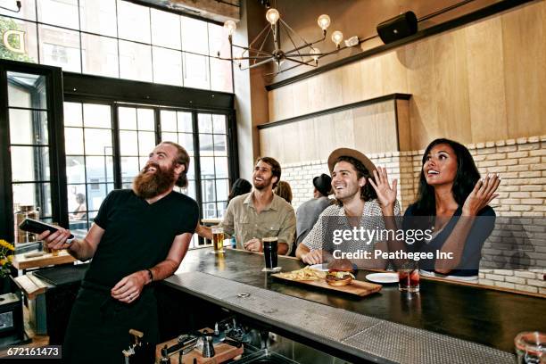 smiling bartender and customers watching television in bar - consumer electronics trade fair stock pictures, royalty-free photos & images