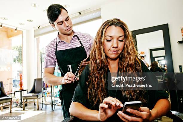 hairdresser with customer texting on cell phone in hair salon - women in suspenders stock-fotos und bilder