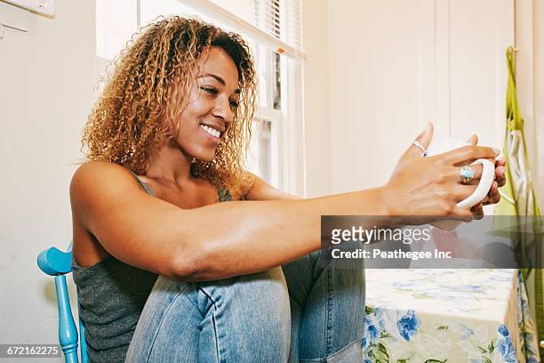 smiling mixed race woman drinking coffee - mixed race woman drinking tea stock-fotos und bilder