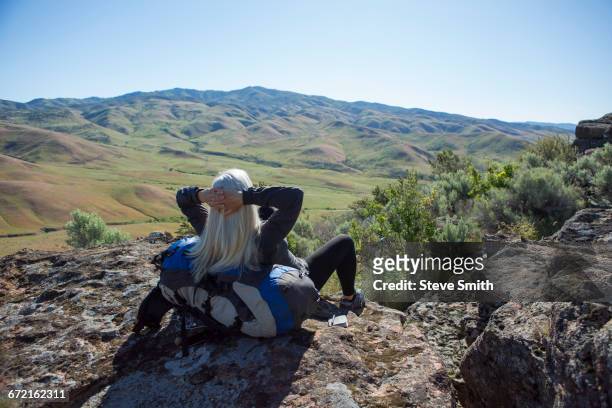 older caucasian woman sitting on rocks leaning on backpack - boise stockfoto's en -beelden